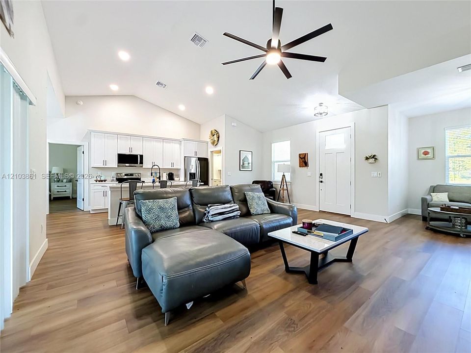 Open floor plan featuring vaulted ceilings, wood-finish flooring, recessed lighting, and a kitchen with white cabinetry and a center island