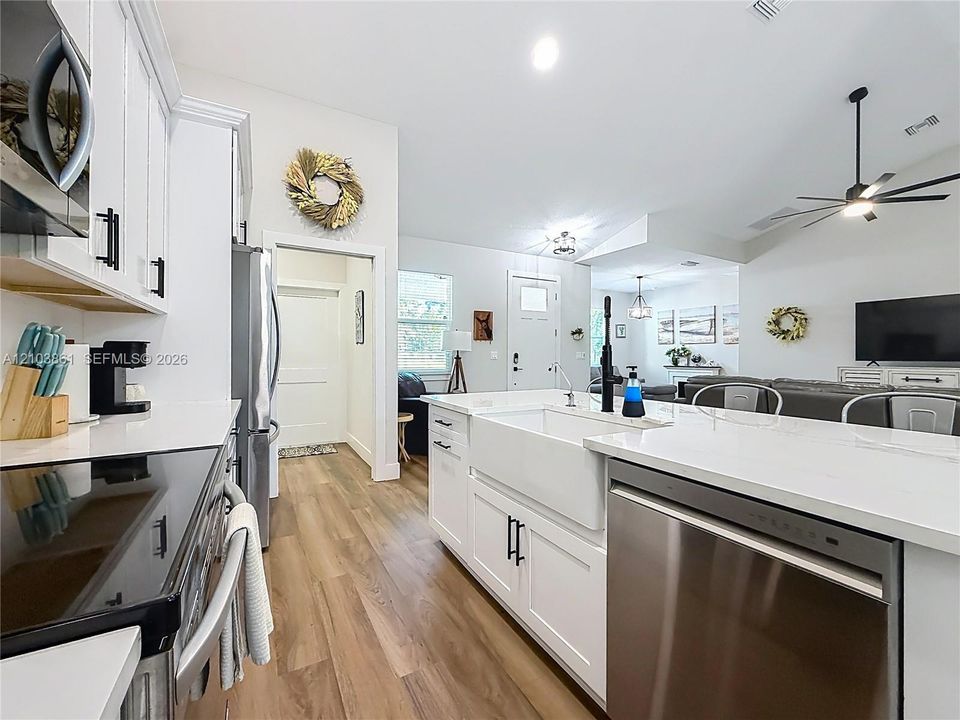 Kitchen featuring white cabinetry, quartz countertops, a farmhouse-style apron sink, matte black hardware, and wood-finish flooring