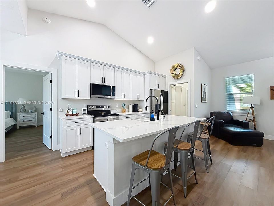 Kitchen featuring white cabinetry, quartz countertops, a central island, stainless steel appliances, and wood-finish flooring under vaulted ceilings