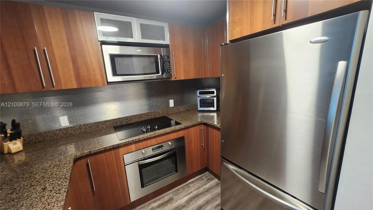 Kitchen featuring wood-finish cabinetry, stone countertops, stainless steel appliances, built-in microwave, and wood-finish flooring