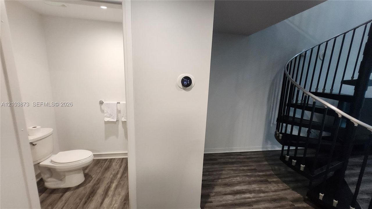 Black metal spiral staircase featuring open risers, wood-finish flooring, smart thermostat, and a porcelain toilet