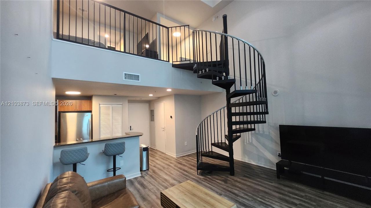Spiral staircase with black metal railing, wood-finish flooring, built-in breakfast bar, and mezzanine level with matching iron railing