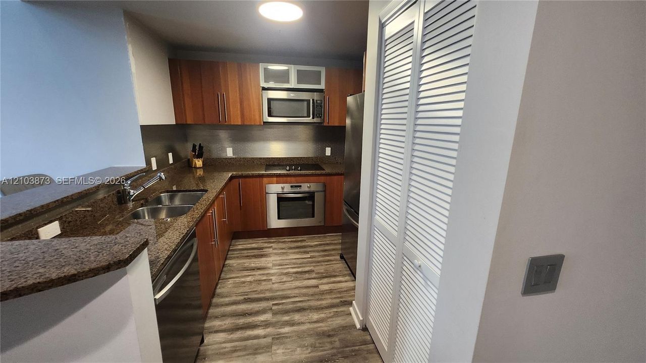 Kitchen featuring wood-finish cabinetry, stone-surface countertops, stainless steel appliances, and wood-finish flooring