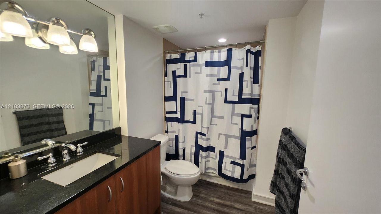 Bathroom featuring a dark stone countertop, integrated sink, wood-finish vanity cabinetry, four-light vanity fixture, and full-width wall mirror