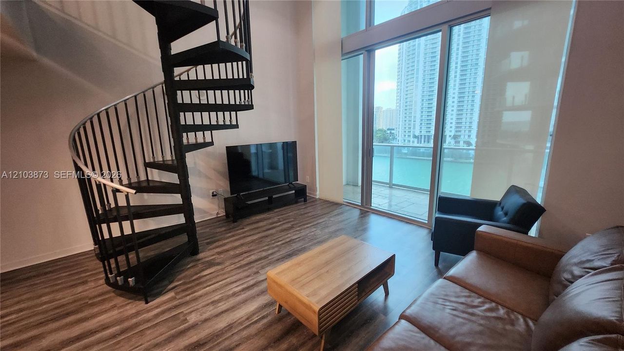 Double-height ceilings featuring floor-to-ceiling windows, wood-finish flooring, and a black metal spiral staircase