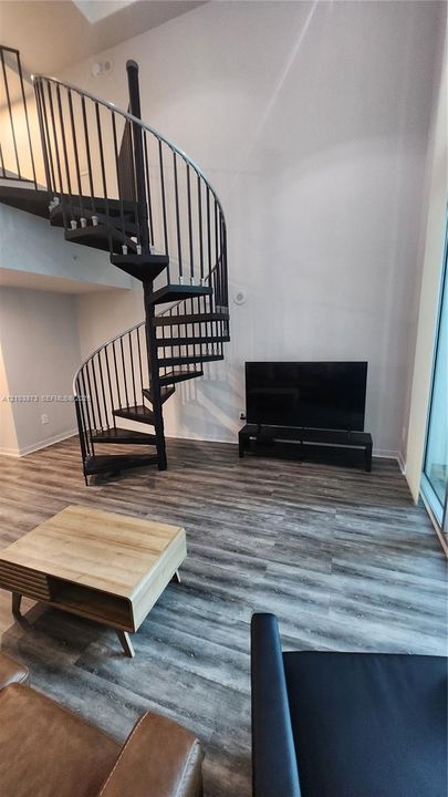 Black metal spiral staircase with high-ceiling clearance and wood-finish flooring
