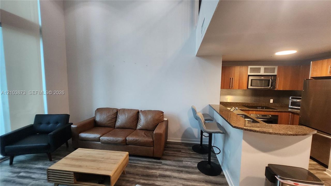 Double-height ceiling, kitchen peninsula with stone-surface countertop, wood-finish flooring, and cabinetry with integrated microwave