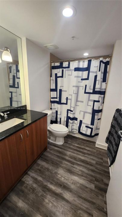 Bathroom featuring a dark stone countertop, integrated sink, wood-finish cabinetry, recessed ceiling lighting, and wood-finish flooring