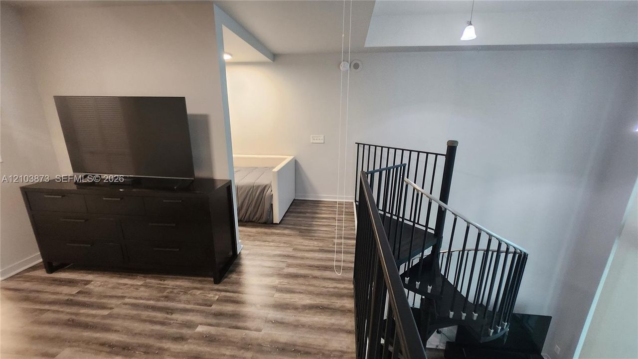 Spiral staircase with matte black metal railings and wood-finish flooring throughout