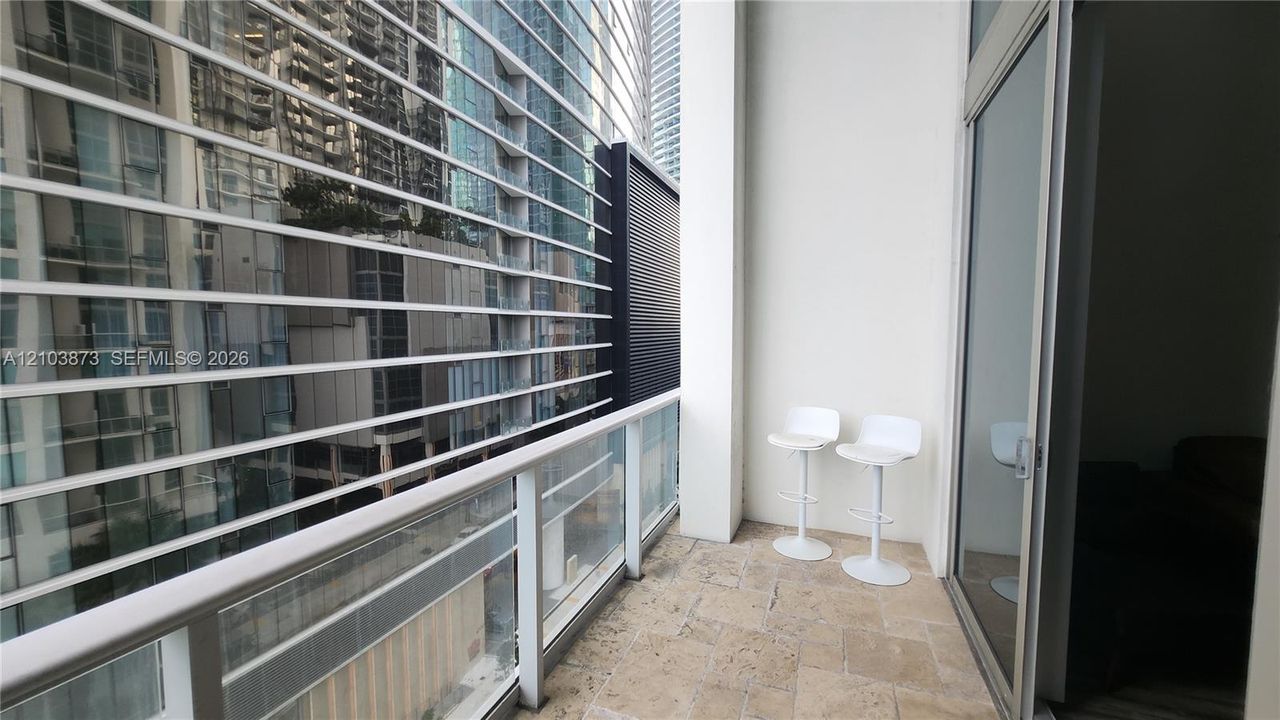 Private covered balcony featuring stone flooring, a glass panel railing, and metal horizontal louvers
