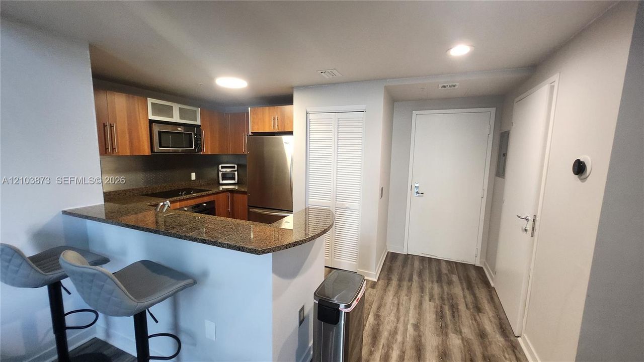 Kitchen featuring wood-finish cabinetry, stone-surface breakfast bar, stainless steel refrigerator, built-in microwave, and wood-finish flooring