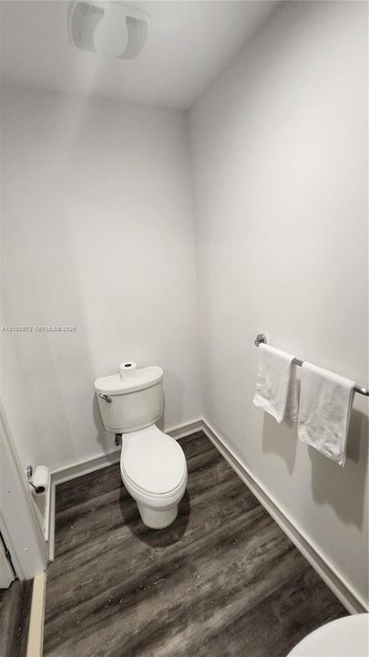 Powder room featuring wood-finish flooring, a white porcelain toilet, and a wall-mounted metal towel rack