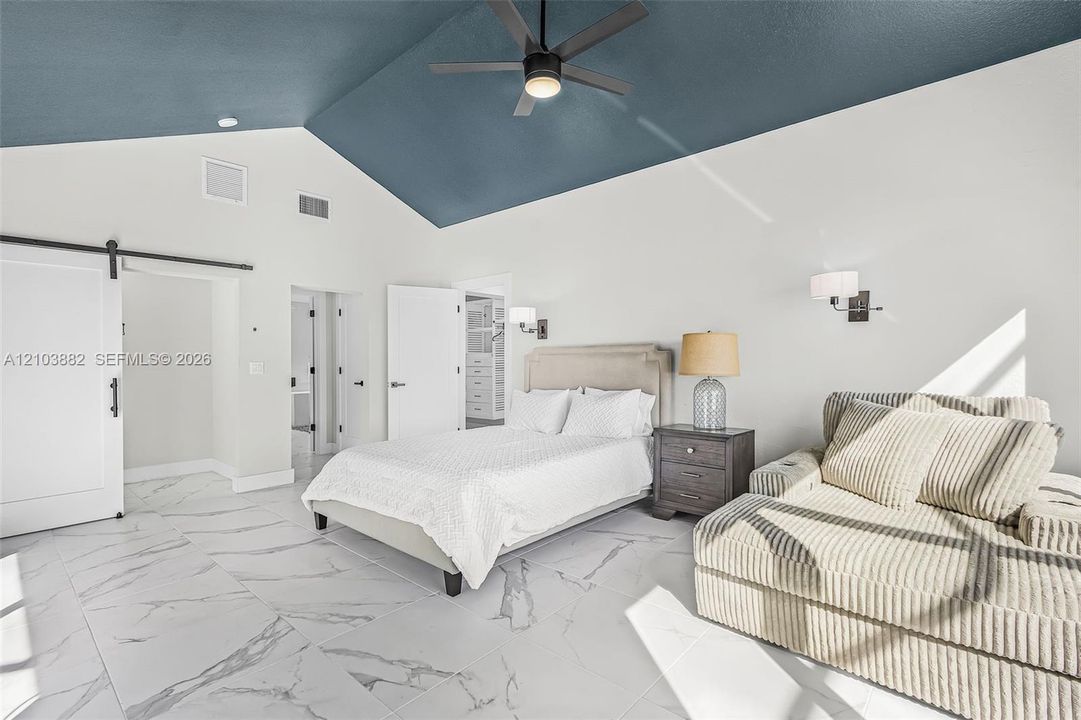 Vaulted ceiling with deep blue accent, large-format stone-finish tile flooring, sliding barn door, and wall-mounted light fixtures