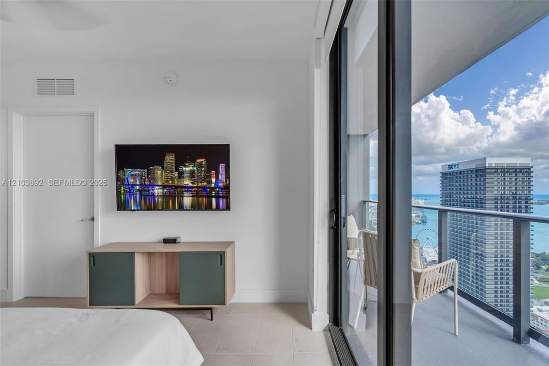 Floor-to-ceiling glass sliding doors, private balcony, neutral large-format tile flooring, and clean-lined contemporary interior finishes