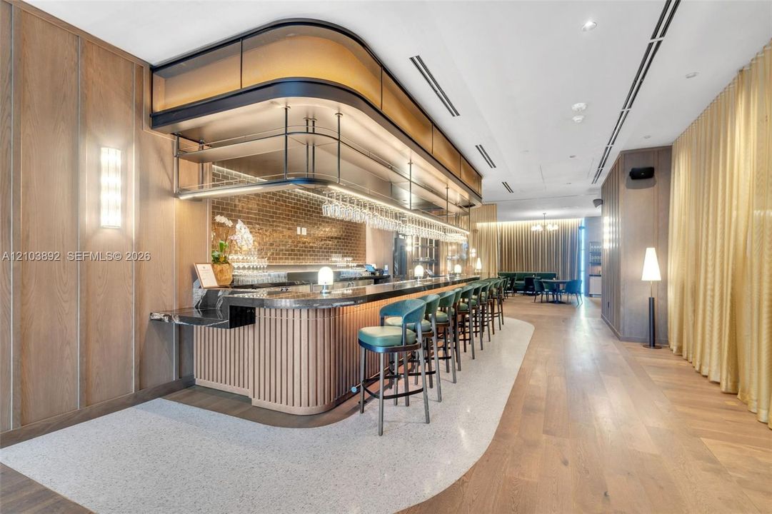 Custom bar featuring a stone countertop, fluted wood detailing, integrated overhead shelving, an exposed brick accent wall, and recessed linear ceiling lighting