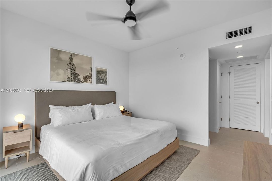 Neutral-toned room featuring a matte black ceiling fan with integrated lighting, tiled flooring, and a multi-panel interior door