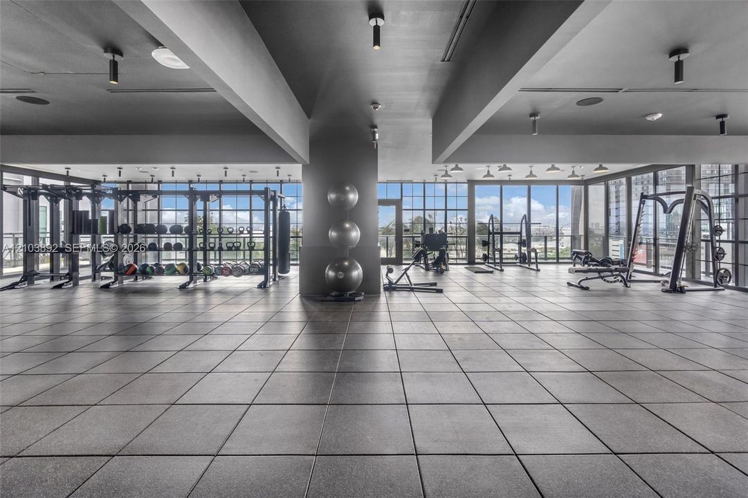 Fitness facility featuring floor-to-ceiling grid windows, large-format tile flooring, exposed structural beams, and recessed ceiling lighting