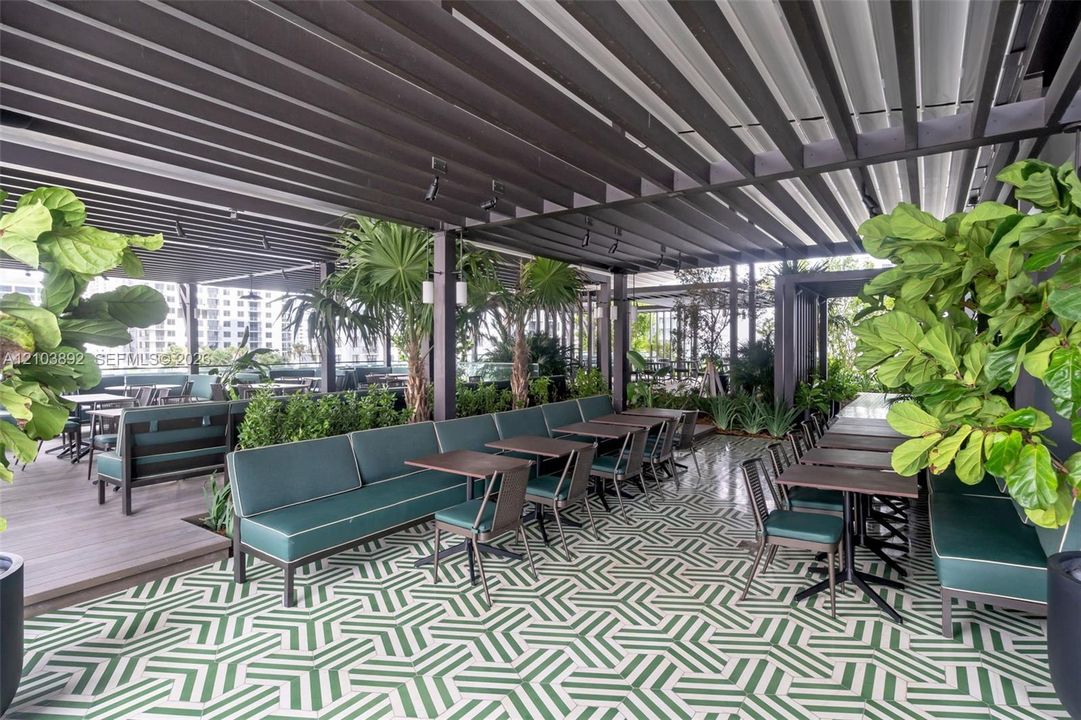 Covered outdoor terrace featuring a black metal louvered pergola, geometric patterned tile flooring, wood-finish decking, integrated track lighting, and built-in perimeter planters