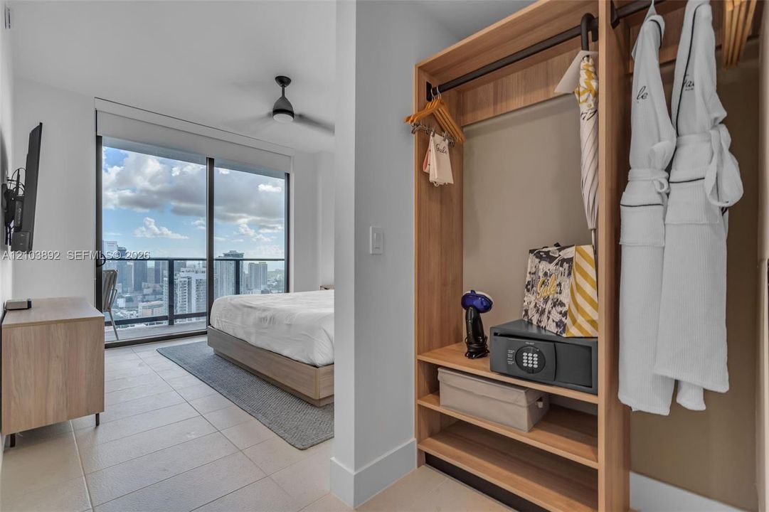 Built-in wood-finish shelving and hanging storage, floor-to-ceiling glass sliding doors, private balcony, ceiling fan, and large-format tile flooring