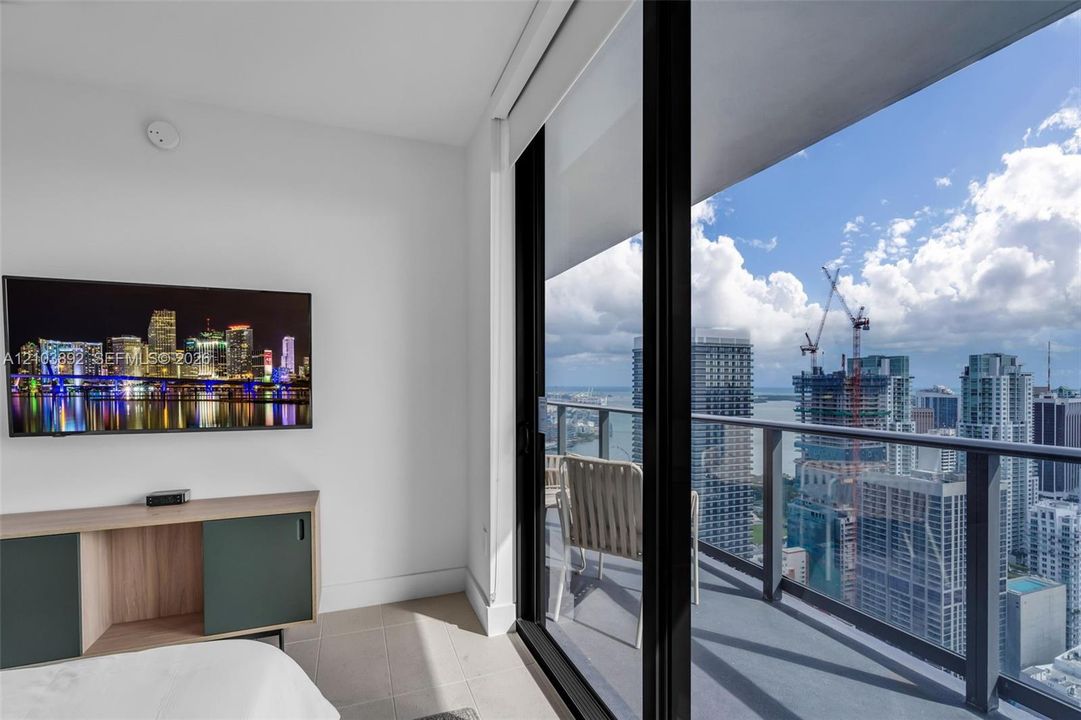 Floor-to-ceiling sliding glass door, private balcony with glass railing, and high-rise urban scenery