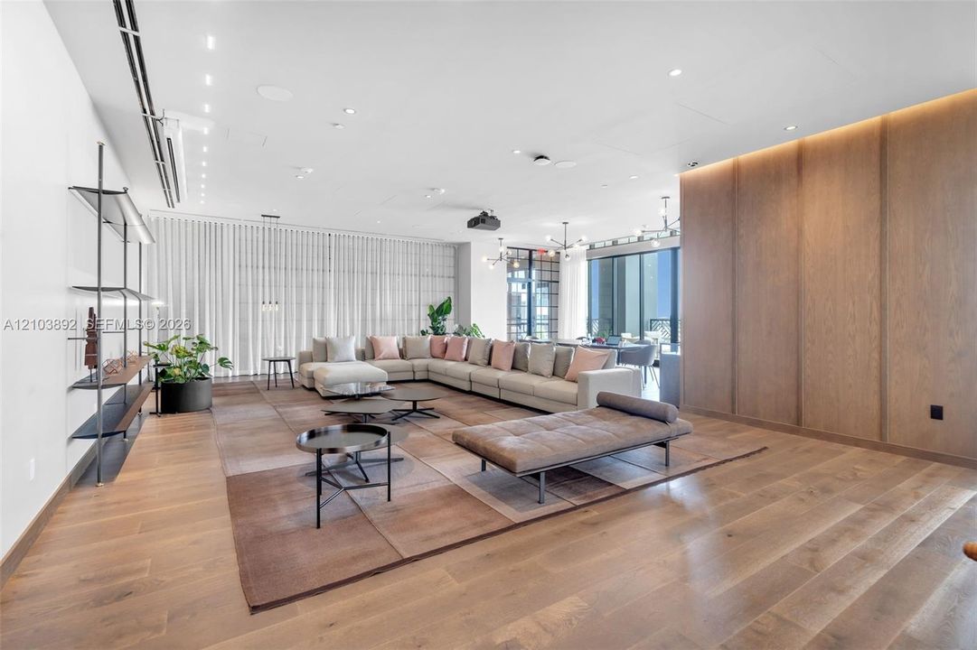 Open-concept living space featuring wood-finish flooring, floor-to-ceiling wood paneling, recessed lighting, and wall-mounted open shelving