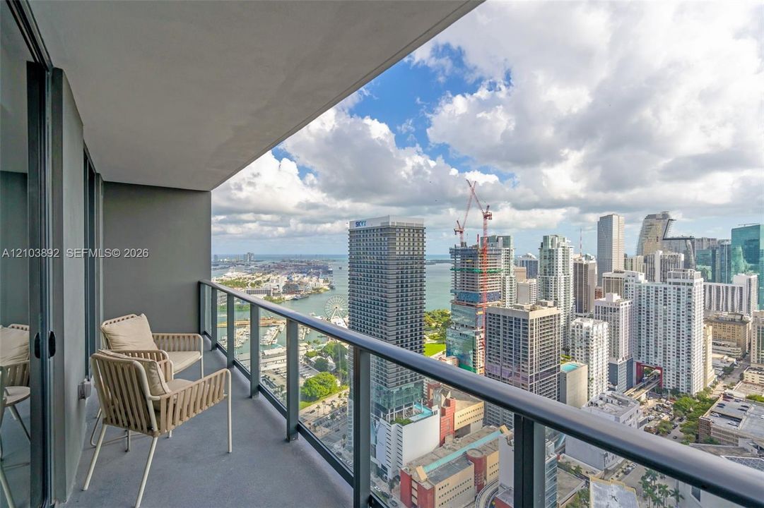 Private balcony featuring a glass-panel railing, painted concrete flooring, and a panoramic urban skyline background