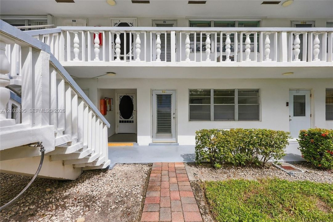 Exterior facade featuring a second-story balcony with balustrade railing, white staircase, brick paver walkway, and horizontal-pane windows