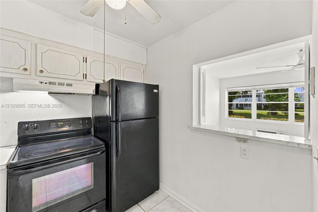 Kitchen featuring black appliances, cabinetry with light-toned finish, tiled flooring, and a pass-through window with a stone-finish ledge