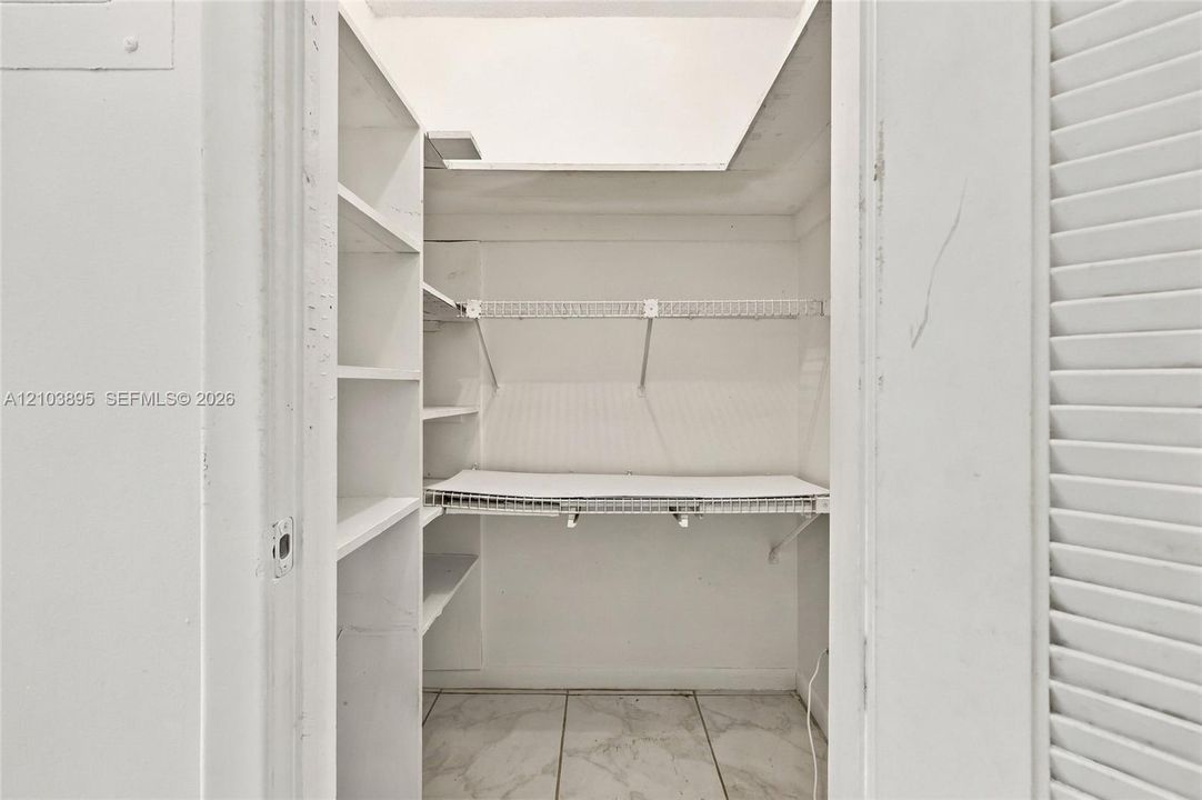 Storage space featuring white built-in shelving, wire racking, and tile flooring