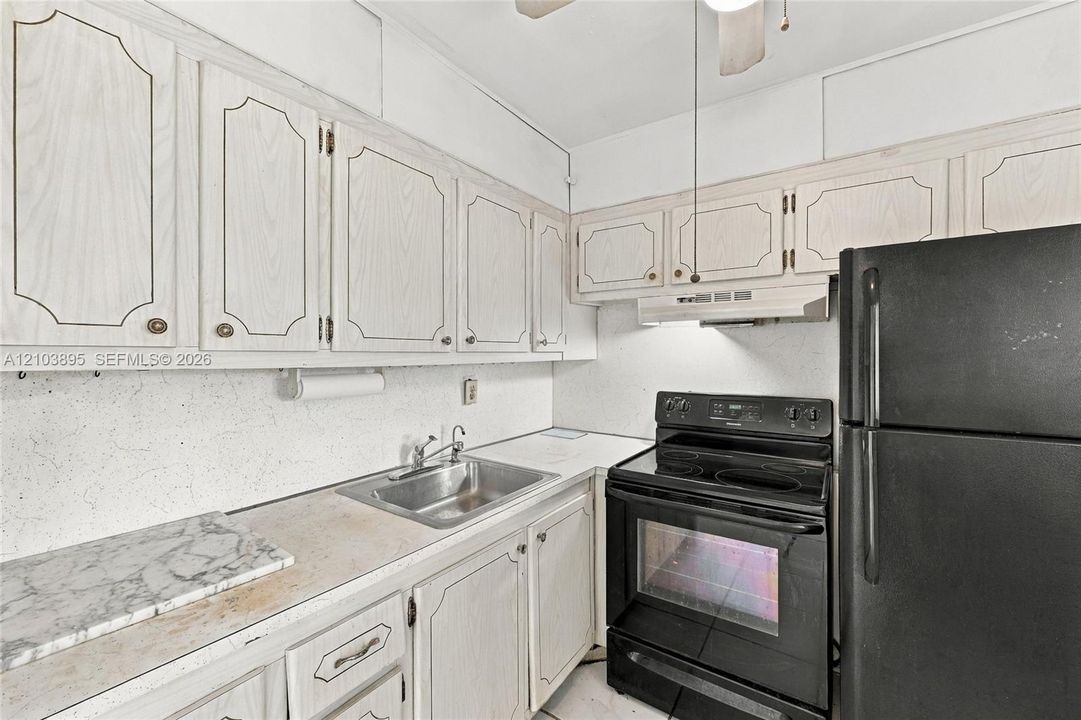 Kitchen featuring light wood-finish cabinetry, stainless steel sink, black range, and black refrigerator