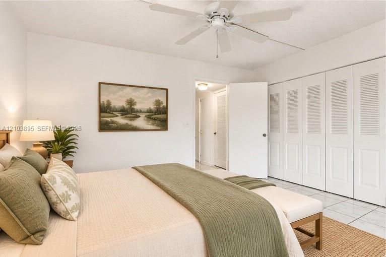 Room featuring a ceiling fan, tiled flooring, and floor-to-ceiling closets with louvered doors