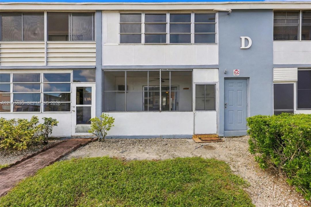 Multi-level exterior featuring a screened-in ground floor patio, large-pane grid windows, solid-surface exterior cladding, and manicured landscaping