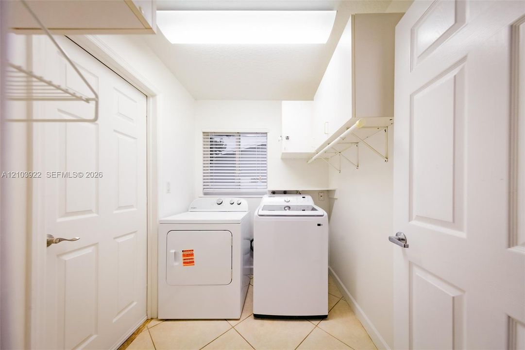 Laundry area with tile flooring, window with blinds, and white cabinetry