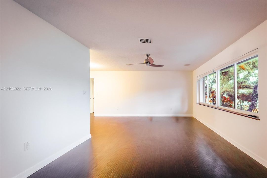 Dark wood-finish flooring, white walls, multiple windows, and a ceiling fan