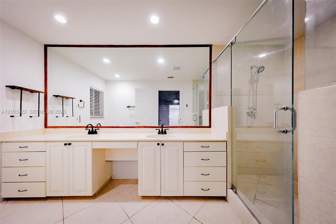 Dual vanity with undermount sinks, expansive mirror, glass-enclosed shower, and built-in cabinetry