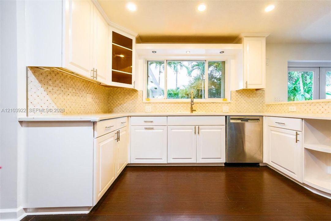 White cabinetry with brushed nickel hardware, light-toned backsplash, stainless steel dishwasher, wood-finish flooring, and recessed lighting
