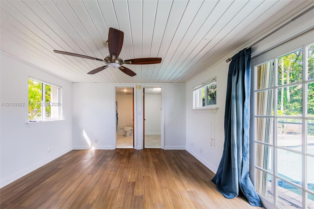 Wood-finish flooring, white plank-style ceiling, dark-finish ceiling fan, and sliding glass doors with a grid pattern