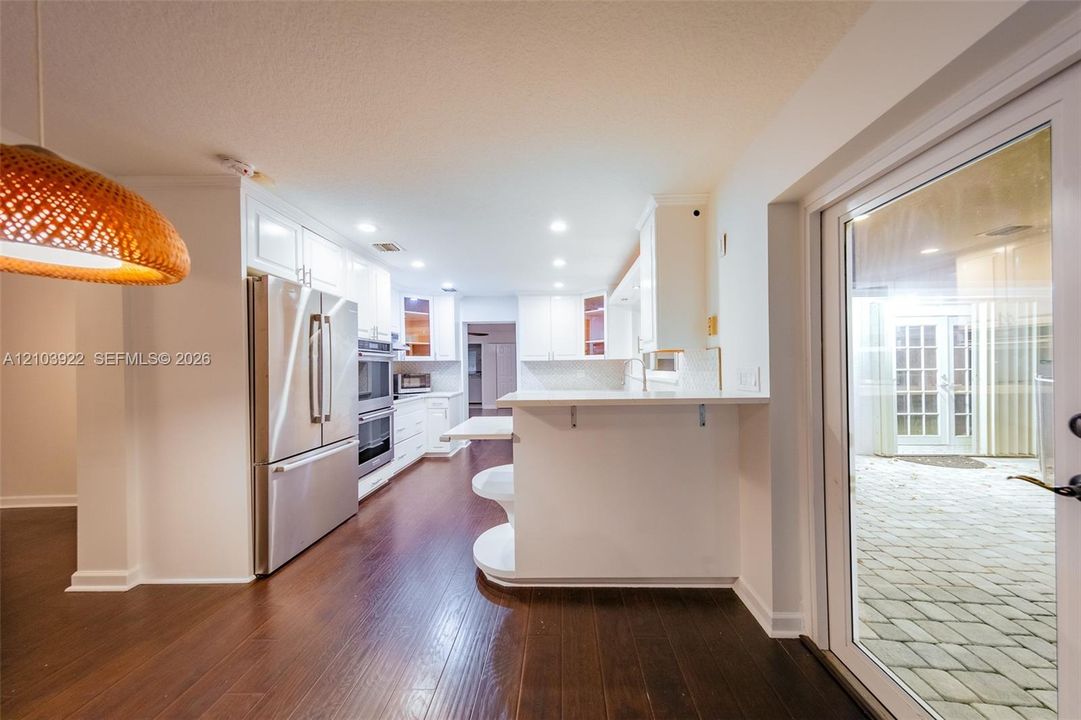 Wood-finish flooring throughout, white cabinetry, stainless steel appliances, recessed lighting, and patio access with glass paneled doors