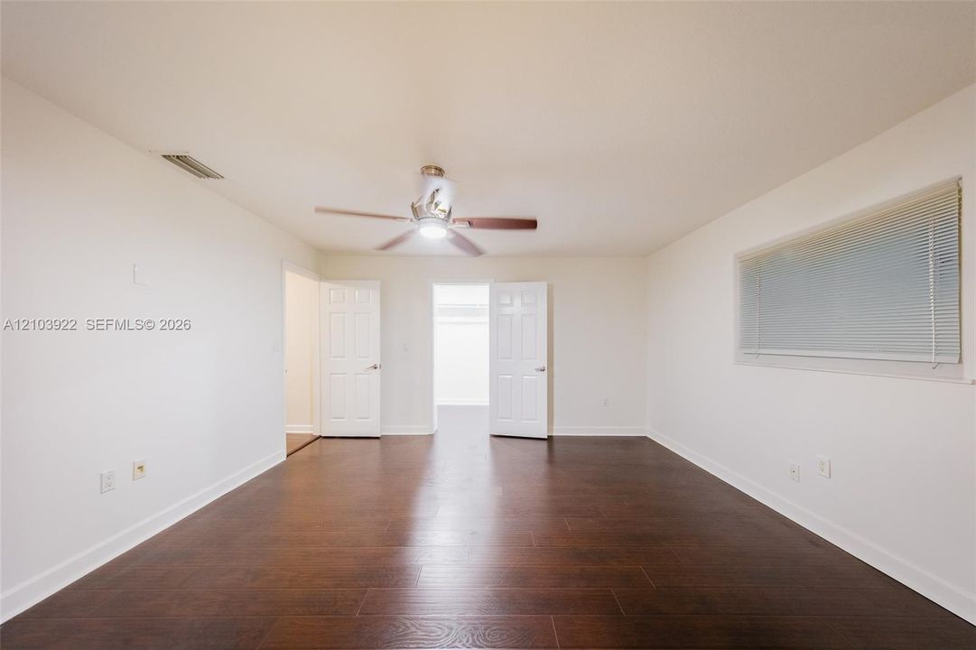 Spacious interior featuring wood-finish flooring, a ceiling fan with integrated lighting, and a large window with blinds