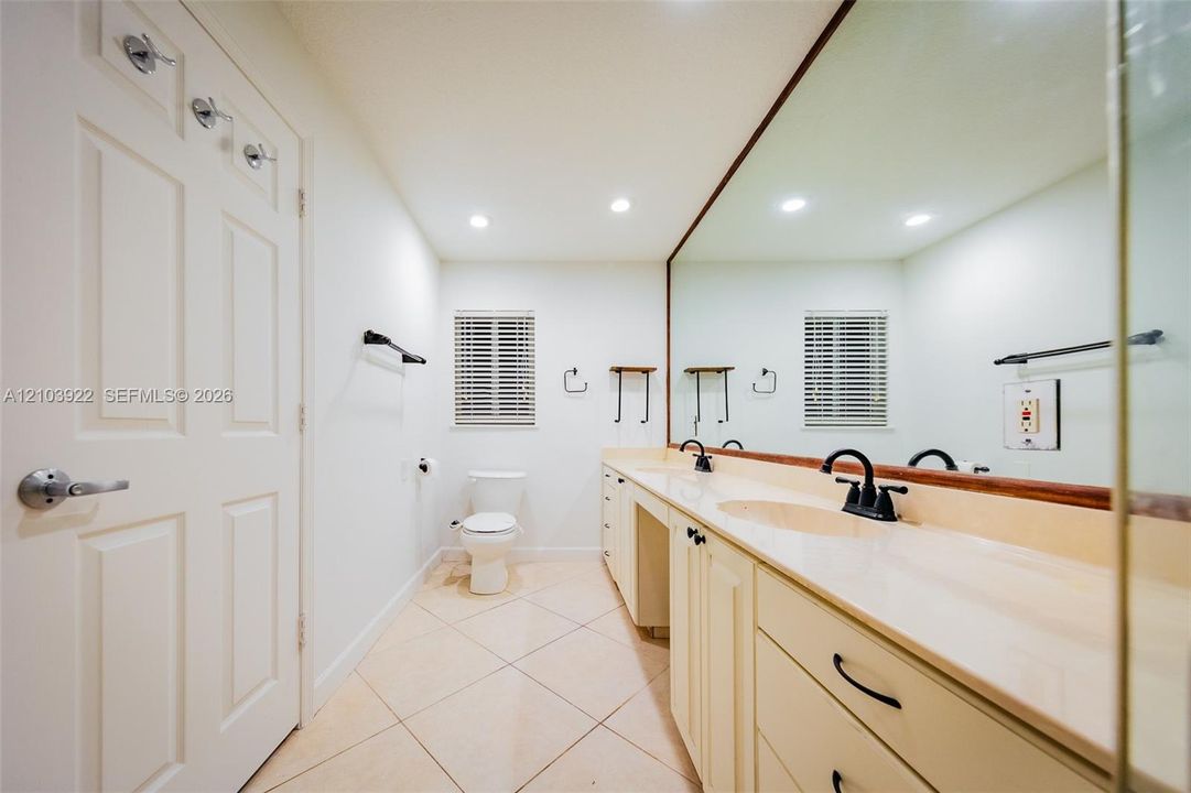 Dual vanity with integrated sinks, recessed lighting, tile flooring, and a large wall-mounted mirror
