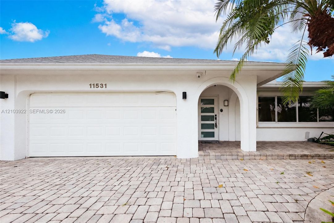 Paver driveway, arched entryway, modern front door, white exterior, attached garage