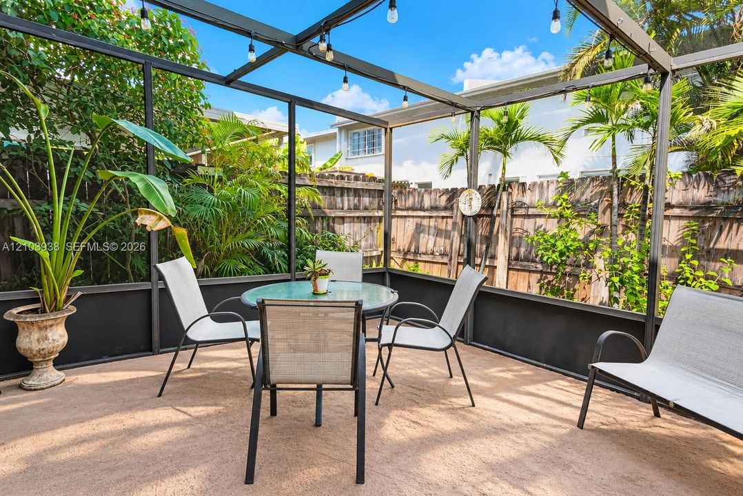 Screened-in patio featuring a concrete floor, metal framing, built-in string lighting, and wood privacy fencing