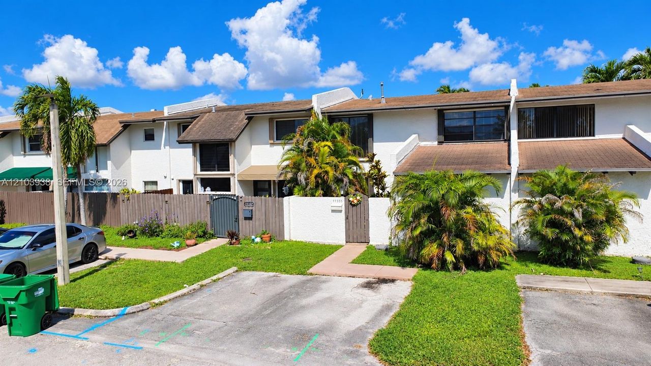 Multi-unit exterior featuring white stucco siding, brown shingle roofing, private fenced courtyards, and dedicated paved parking
