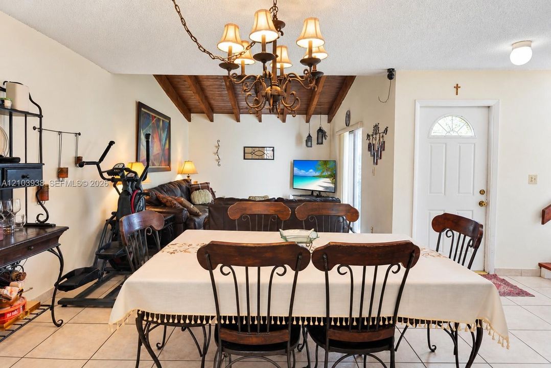 Vaulted ceiling with exposed wood beams, multi-arm chandelier, and ceramic tile flooring