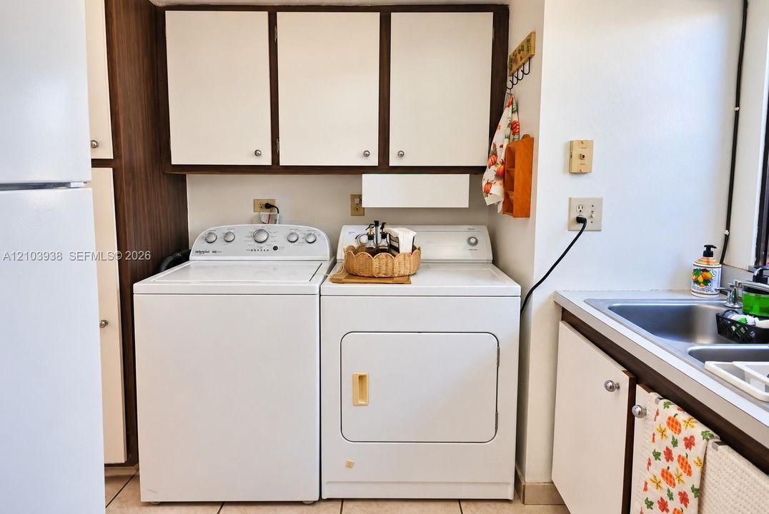 Laundry area featuring overhead cabinetry, built-in dual-basin stainless steel sink, and ceramic tile flooring