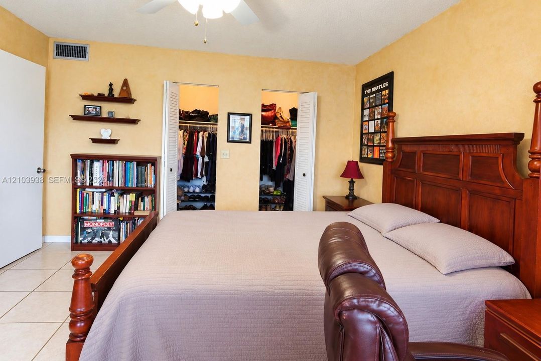Room interior featuring neutral wall paint, tile flooring, dual closets with louvered doors, and a ceiling-mounted fan