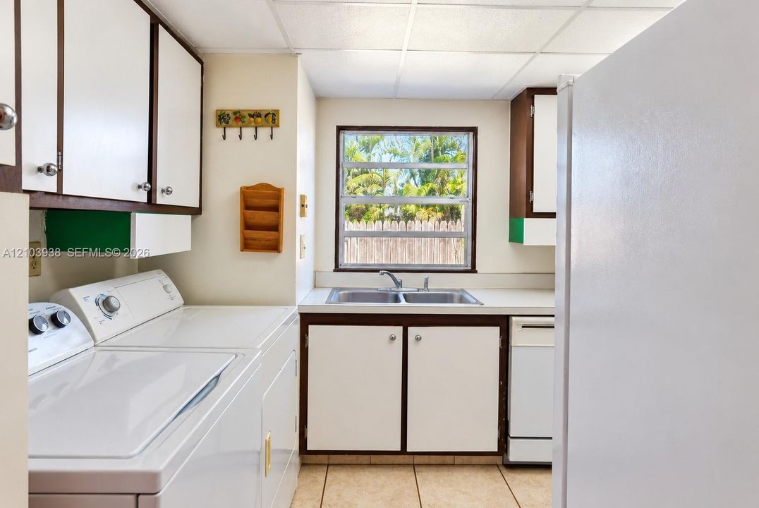 Laundry area featuring white cabinetry with dark trim, a stainless steel dual-basin sink, tile flooring, and a window providing natural light