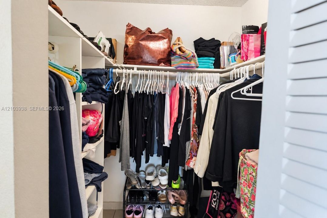 Walk-in closet featuring white built-in shelving and tiered hanging rods
