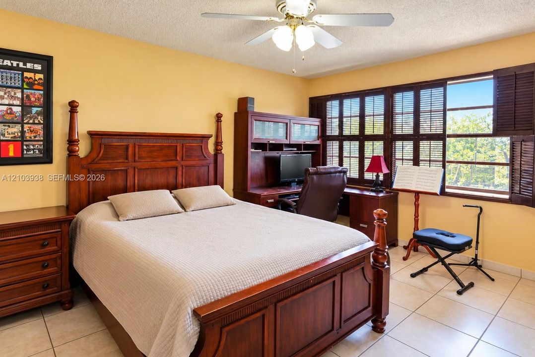 Tile flooring, wood-finish built-in desk unit, ceiling fan with light fixture, and windows featuring attached dark wood shutters