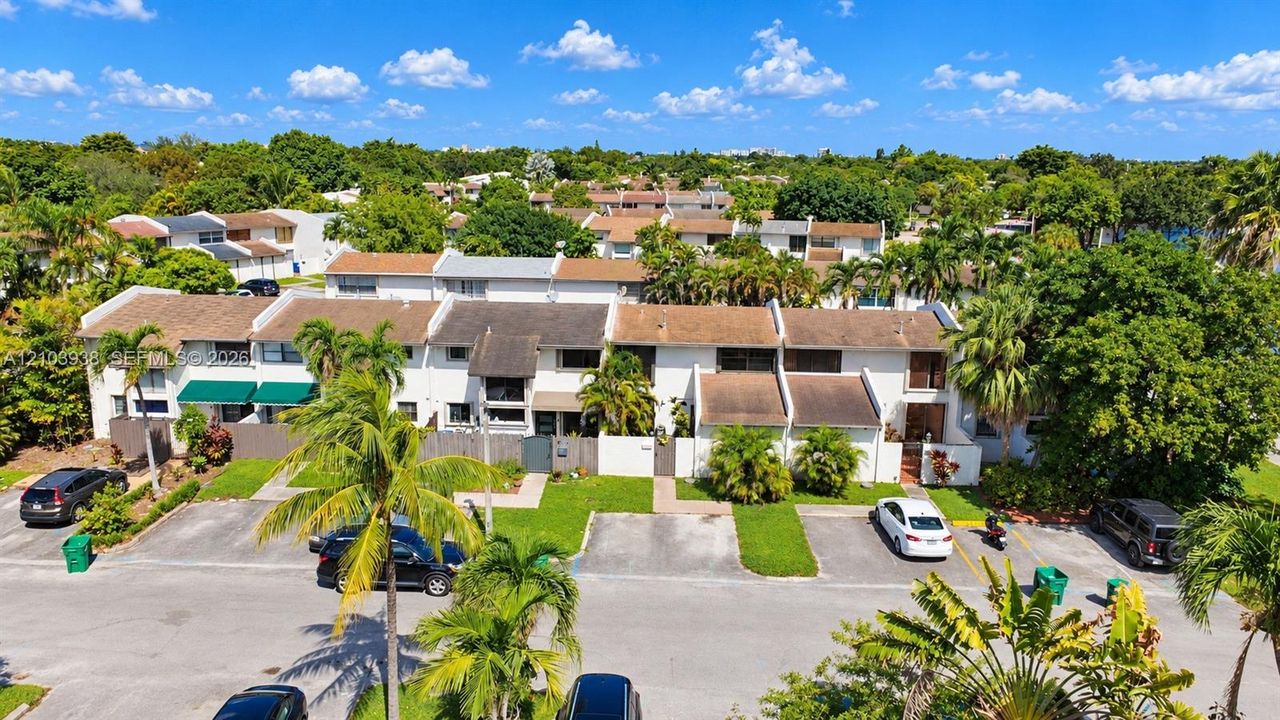 Multi-level townhome exterior featuring a neutral stucco facade, individual private entrance courtyards, pitched shingle roofing, and dedicated surface parking